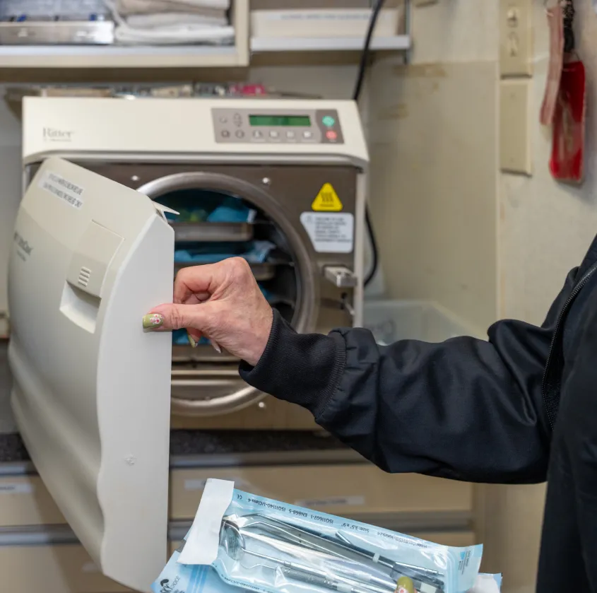 Hand opening autoclave sterilizer with sterilized dental tools in blue packaging.