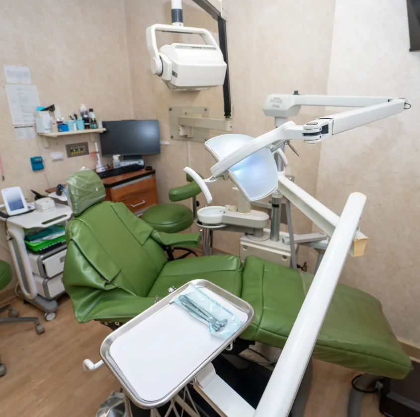 Empty green dental chair with equipment in a clean dental clinic room.