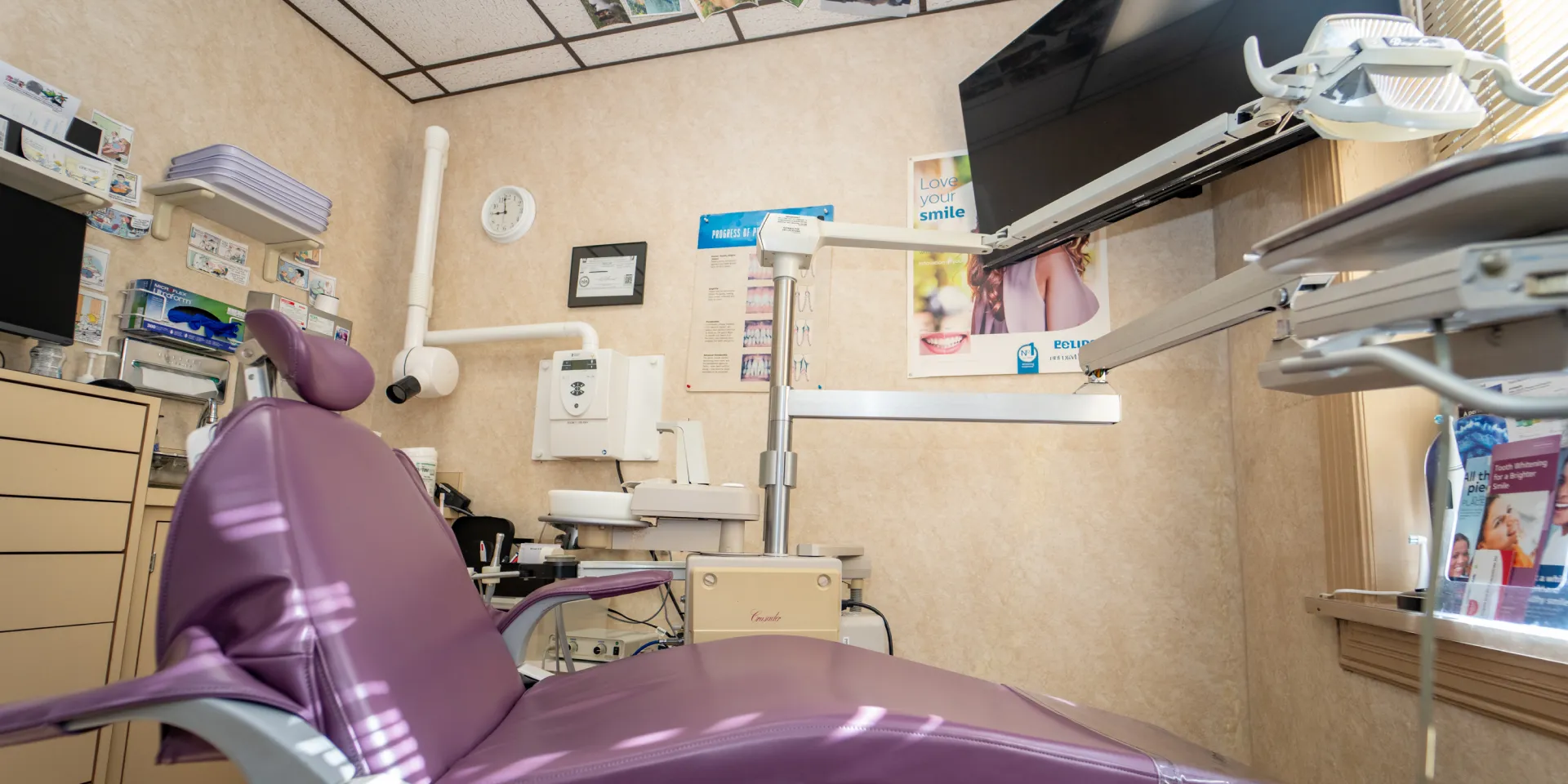 Purple dental chair with dental equipment and posters in a well-lit dental office room.