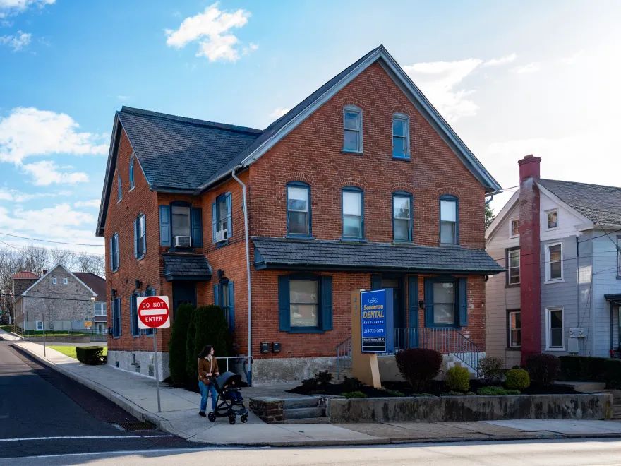 Red brick two-story building with a dental office sign and a woman pushing a stroller on sidewalk.