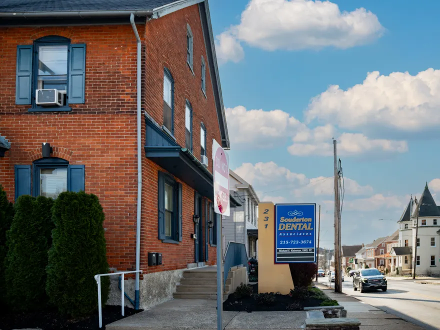Brick building with blue shutters and a sign for Souderton Dental Associates on a sunny street.