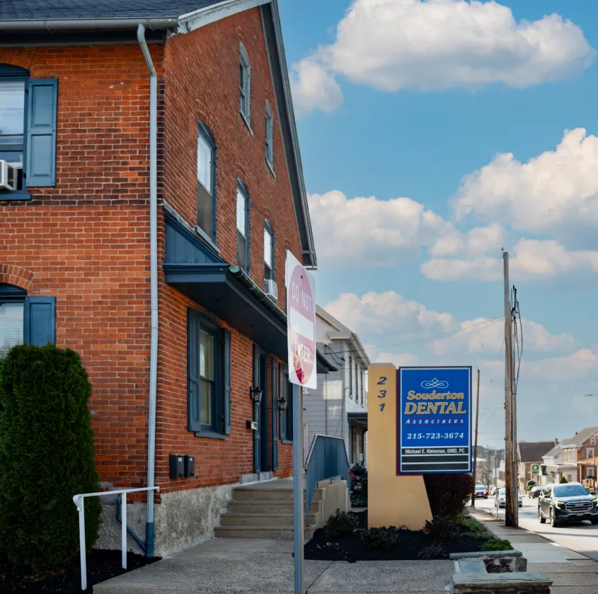 Brick building with blue trim and sign for Souderton Dental Associates at 231 on a clear day.