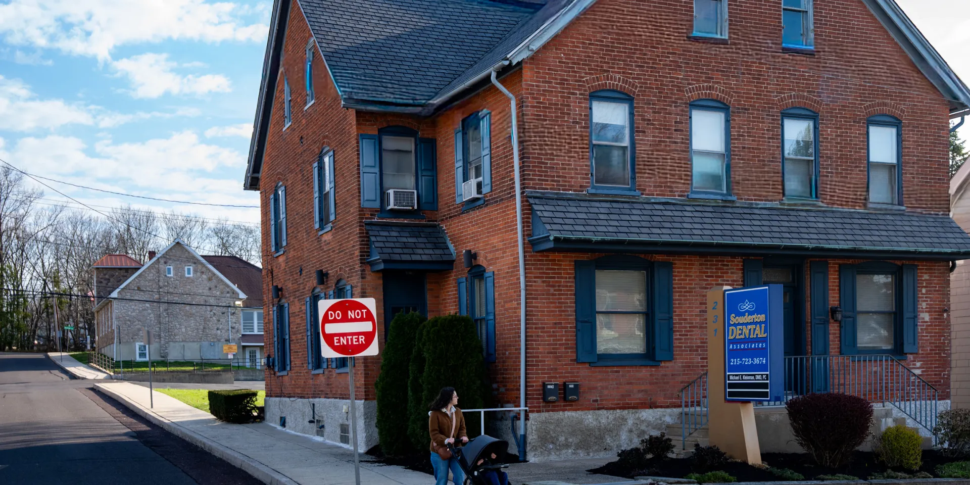 Brick dental office building with blue trim, a Do Not Enter sign, and a woman pushing a stroller nearby.