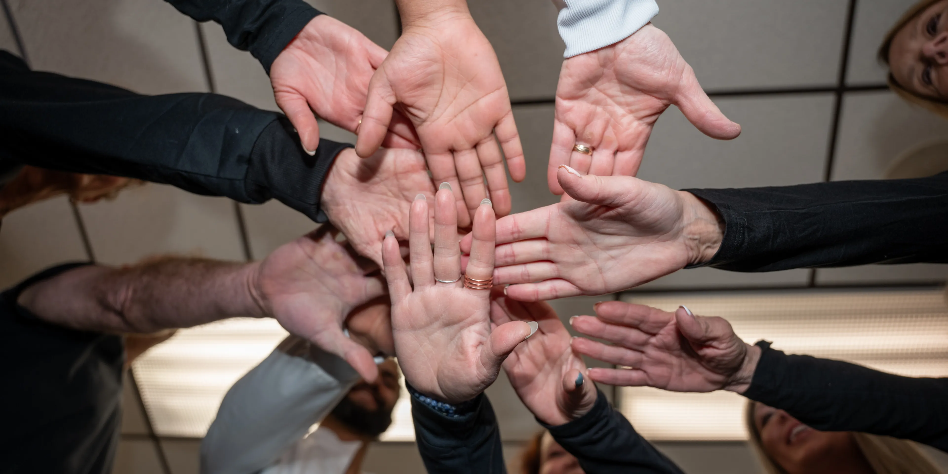 Group of people in a circle putting their hands together in a team-building gesture.
