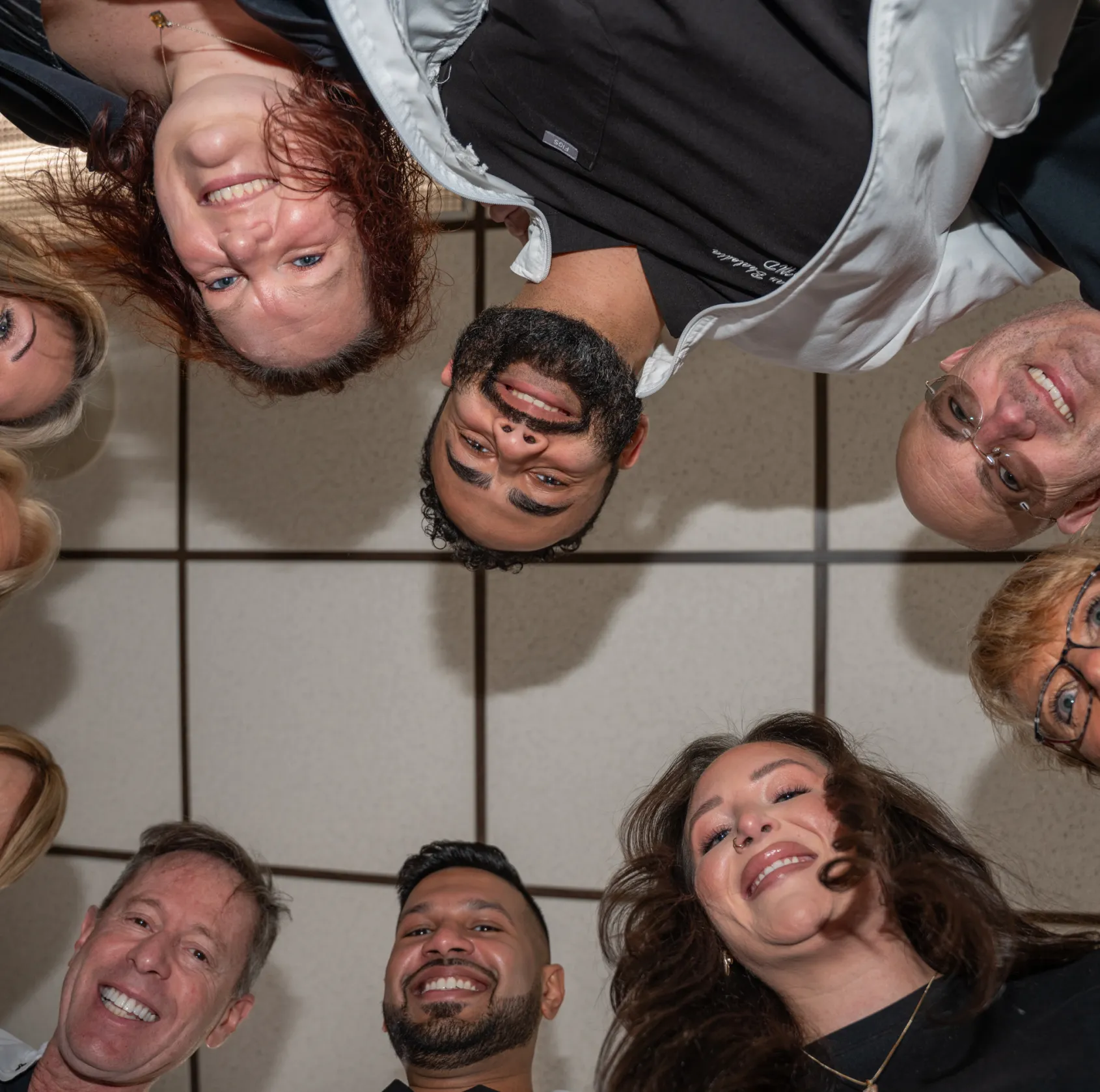 Group of diverse smiling people in a circle looking down at the camera in an indoor setting.