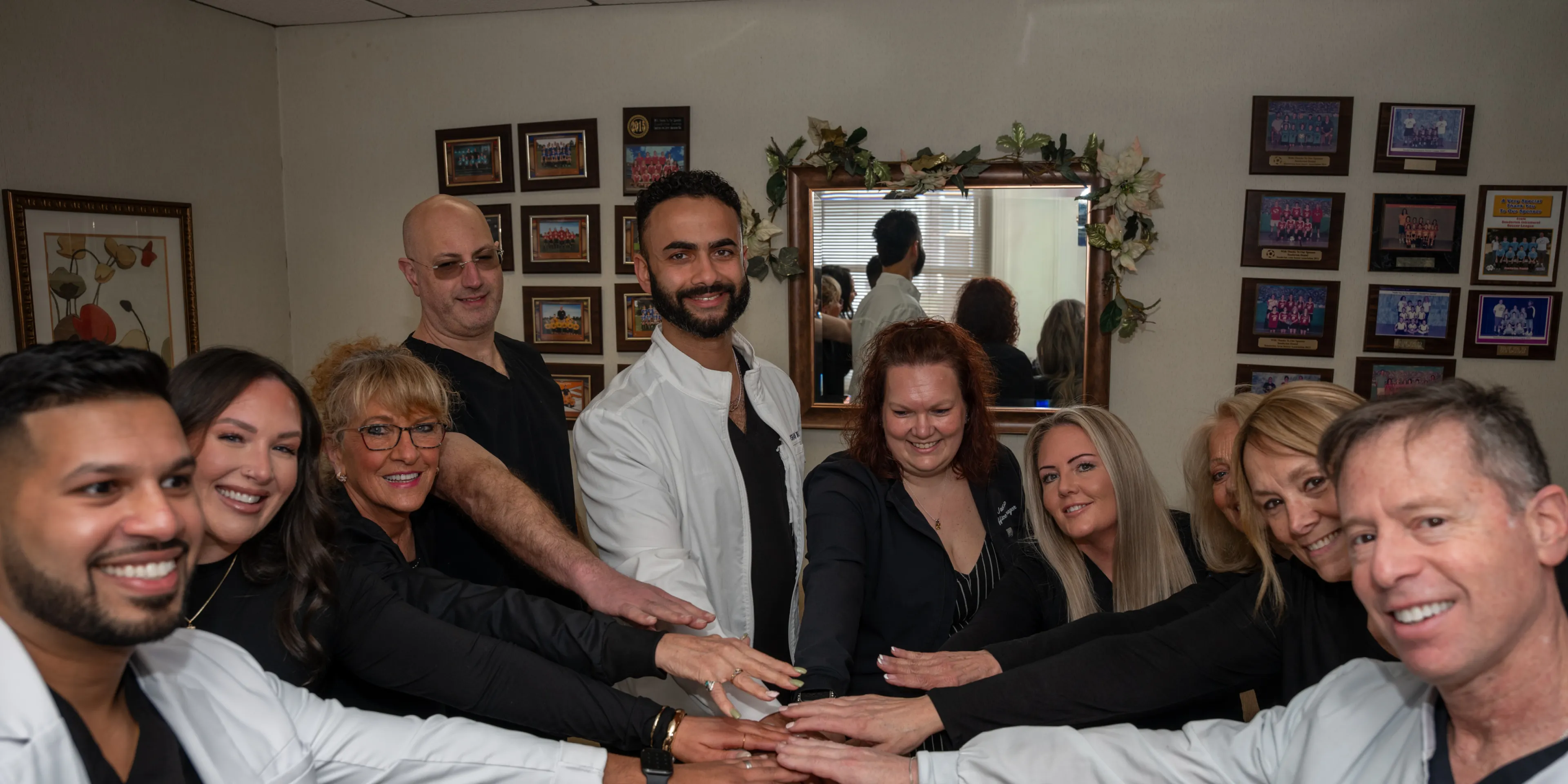 A diverse group of medical staff smiling and joining hands in a teamwork gesture in a room.
