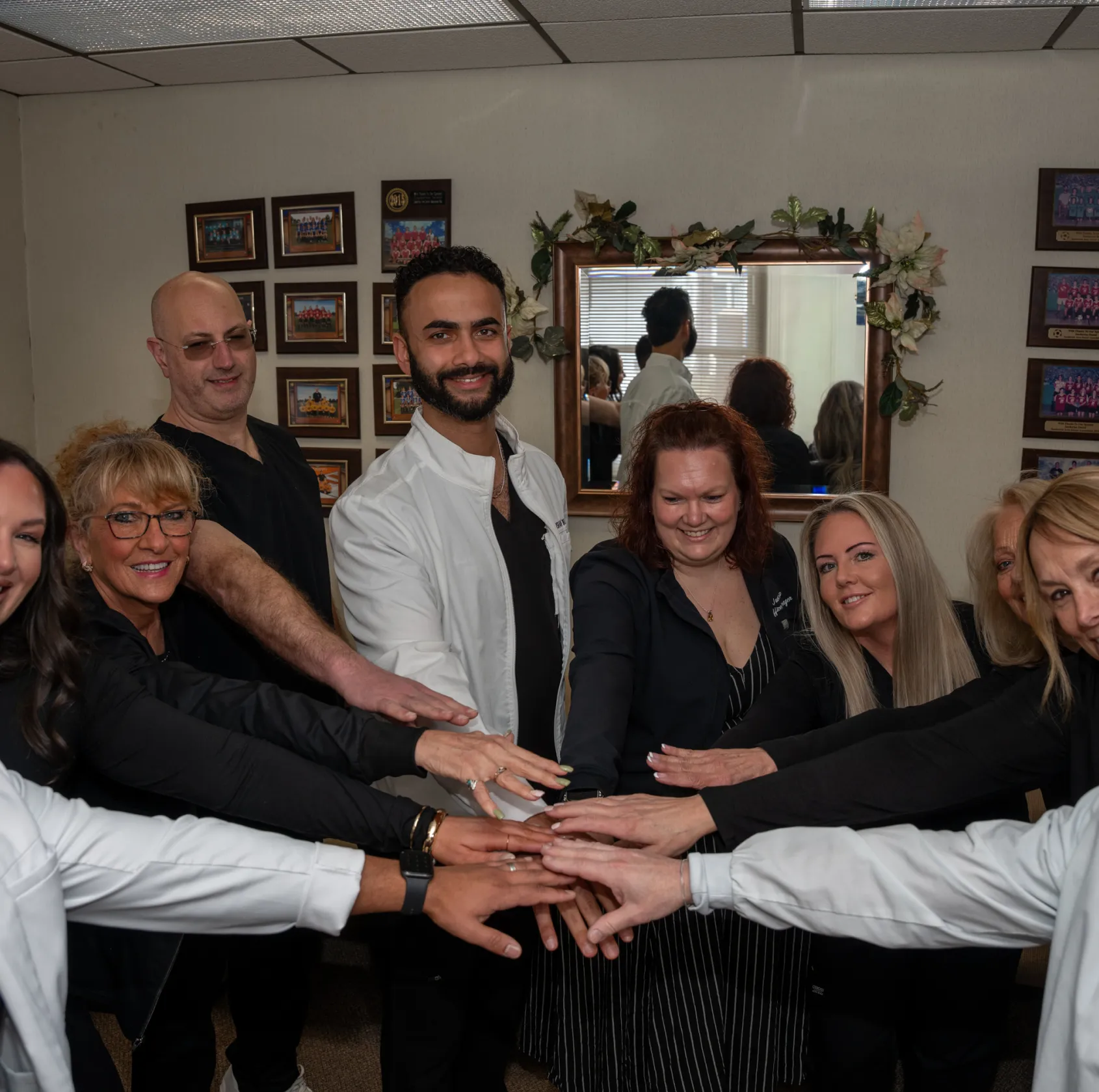Group of smiling people in an office putting their hands together in a team huddle.