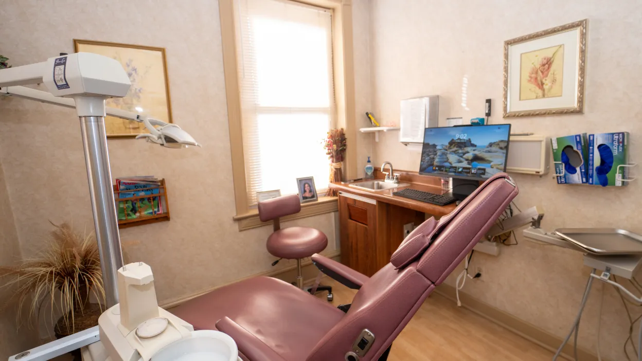 Dental chair and equipment in a clean, well-lit dental exam room with computer and sink.
