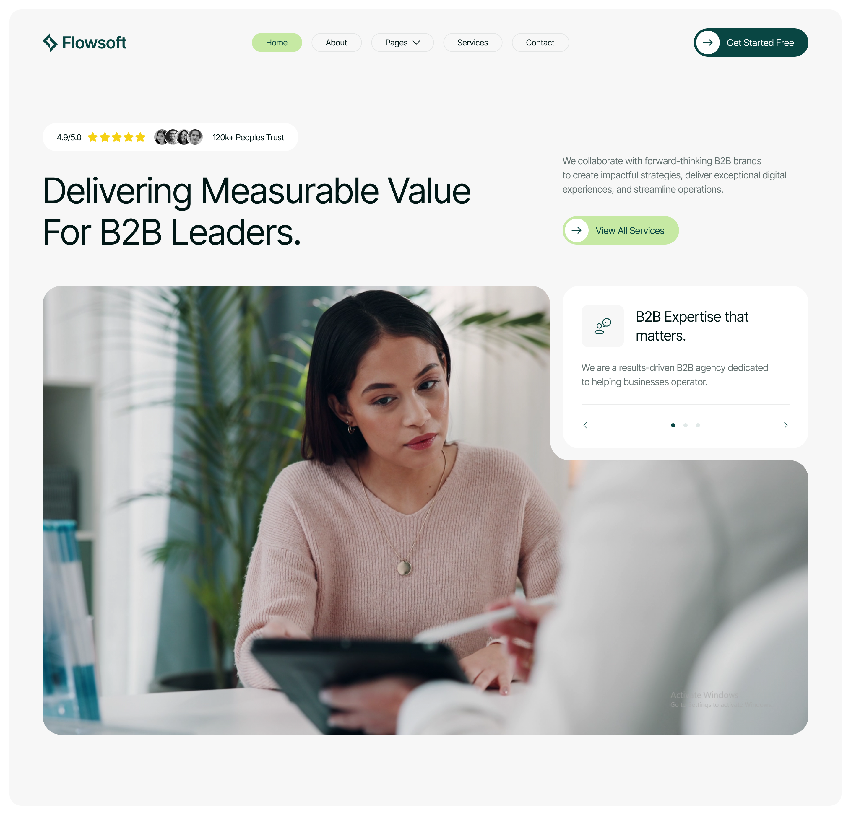 Woman in a pink sweater attentively looking at a tablet held by a person pointing with a stylus in a modern office setting.