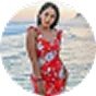 Woman in a red floral dress standing in front of a body of water during sunset.