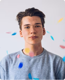 Young man with short dark hair wearing a gray sweater with colorful confetti falling around him.