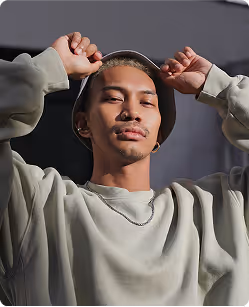 Young man wearing a light hoodie and silver chain, adjusting the hood with both hands.