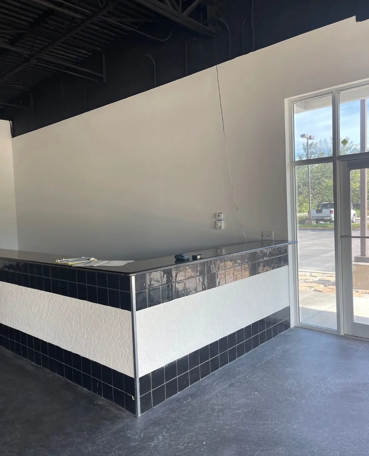 Commercial buildout counter with tiled front, unfinished ceiling, and natural light from storefront windows