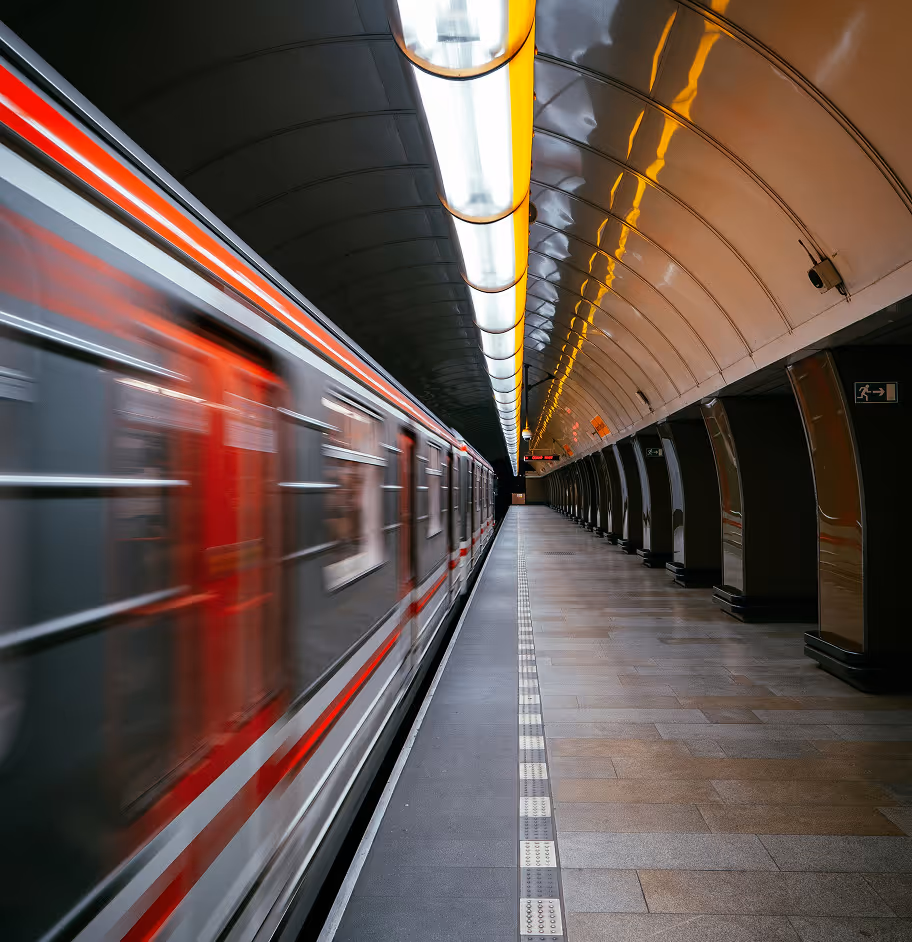 Stanice metra s širokou perilovou podlahou, visícími ukazateli směrů a vlakem stojícím na levé koleji.