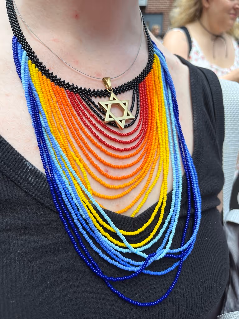 Close-up of a person wearing a rainbow-colored beaded necklace with a gold Star of David pendant.