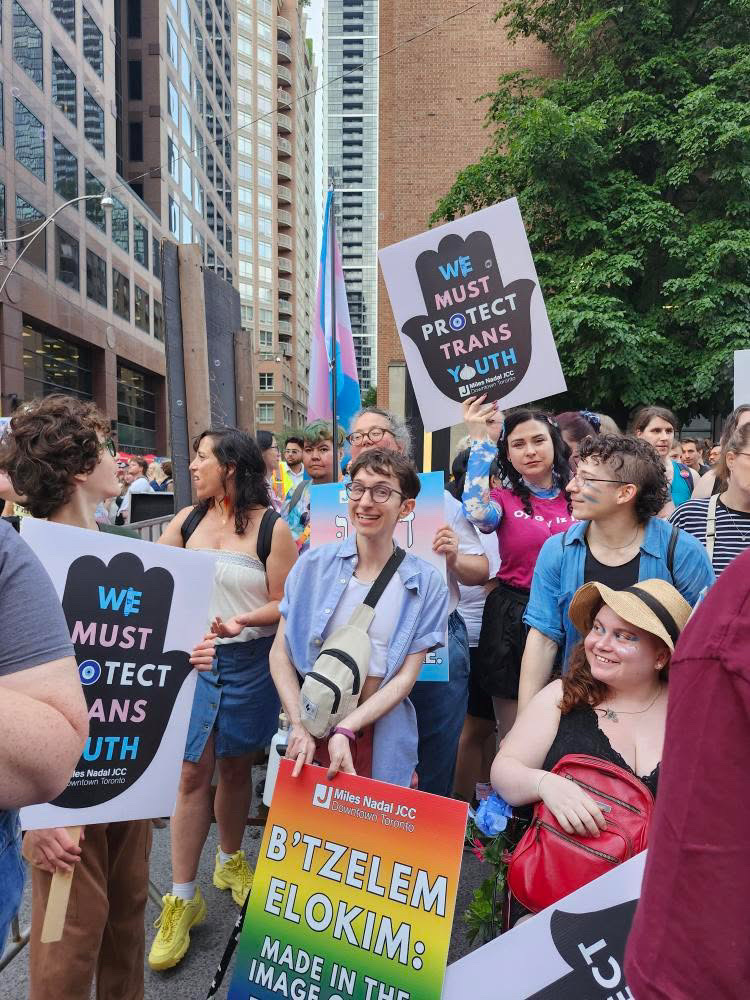 Group of people at a pride march holding signs supporting trans youth and equality in an urban setting.