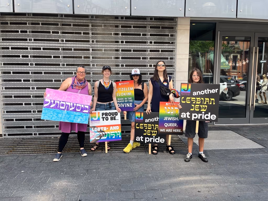 Five people standing outdoors holding colorful signs with LGBTQ+ and Jewish pride messages in English and Hebrew.