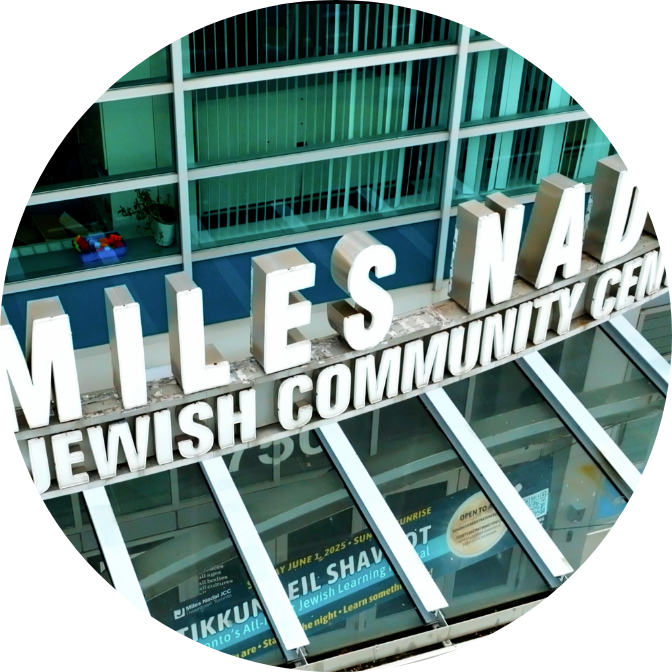 Exterior sign reading 'Miles Nadal Jewish Community Center' above glass entrance with event posters visible inside.