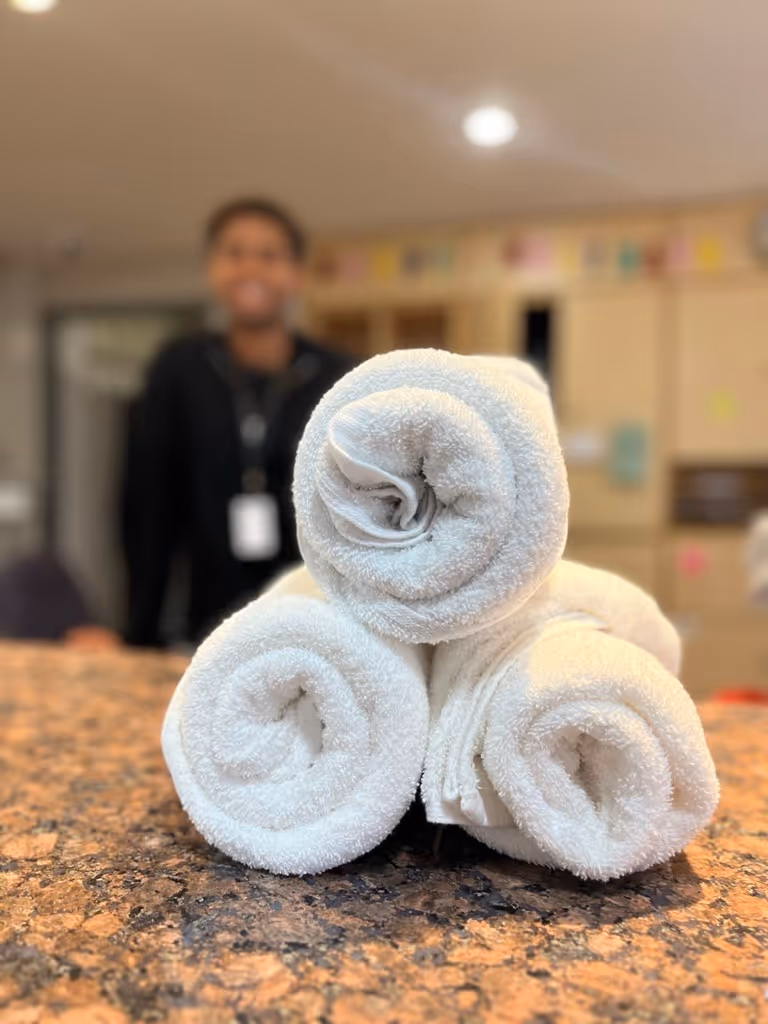 Three white rolled towels stacked in a pyramid shape on a granite countertop with a blurred person in the background.
