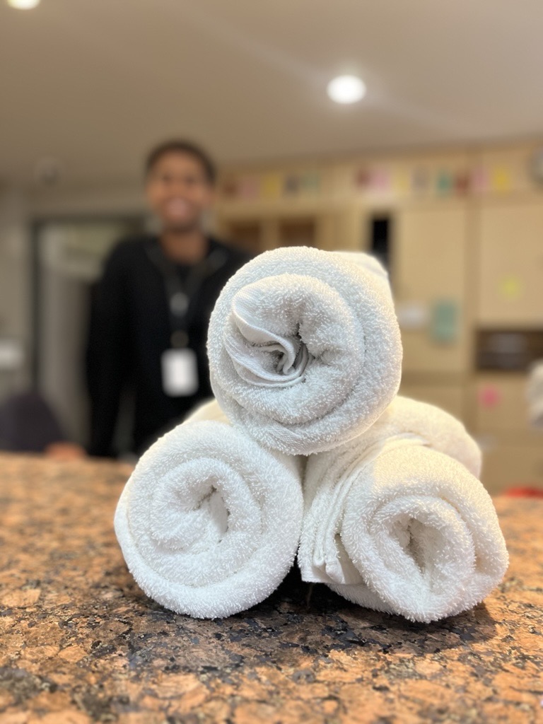 Three white rolled towels stacked in a pyramid shape on a granite countertop with a blurred person in the background.
