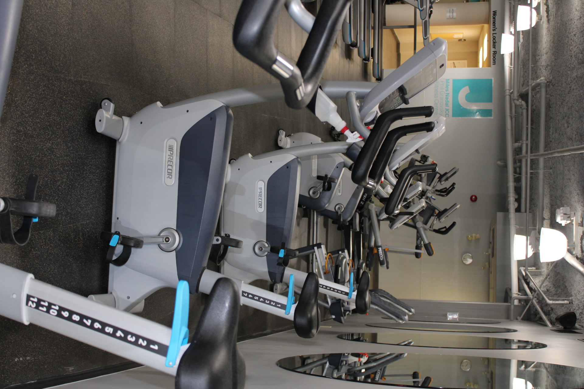 Row of Precor stationary exercise bikes lined up in a gym with mirrors reflecting the equipment.