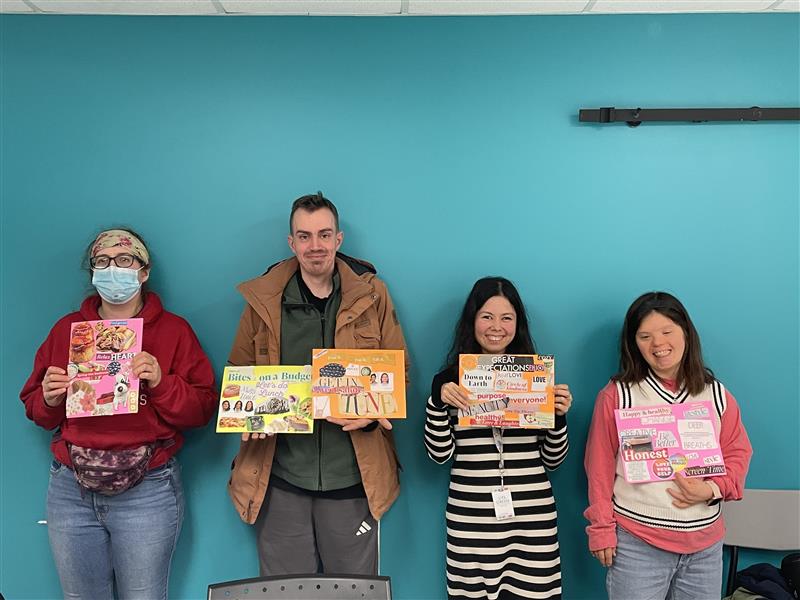 Four people standing against a teal wall, each holding a colorful collage poster with words and images.