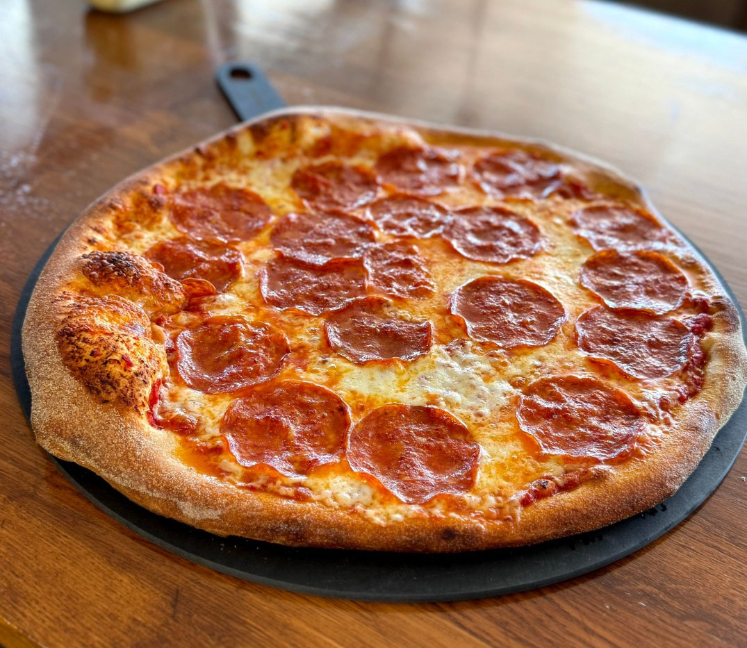 A freshly baked pepperoni pizza with a golden crust, melted cheese, and evenly spread pepperoni slices on a wooden table.