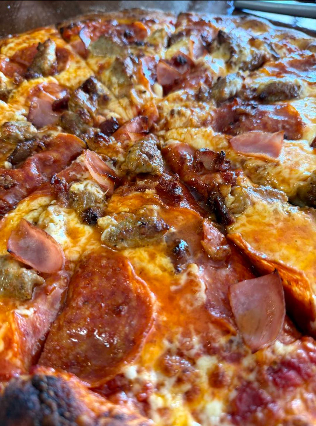 Close-up of a pizza loaded with pepperoni, sausage, and ham.