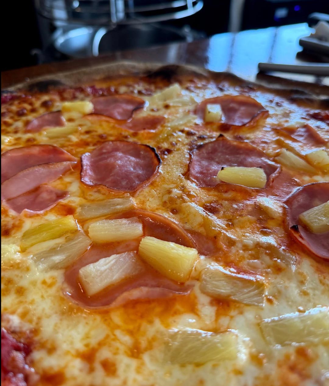 Close-up of a pizza featuring ham and pineapple chunks atop a golden-brown crust, suggesting a savory and sweet Hawaiian style.