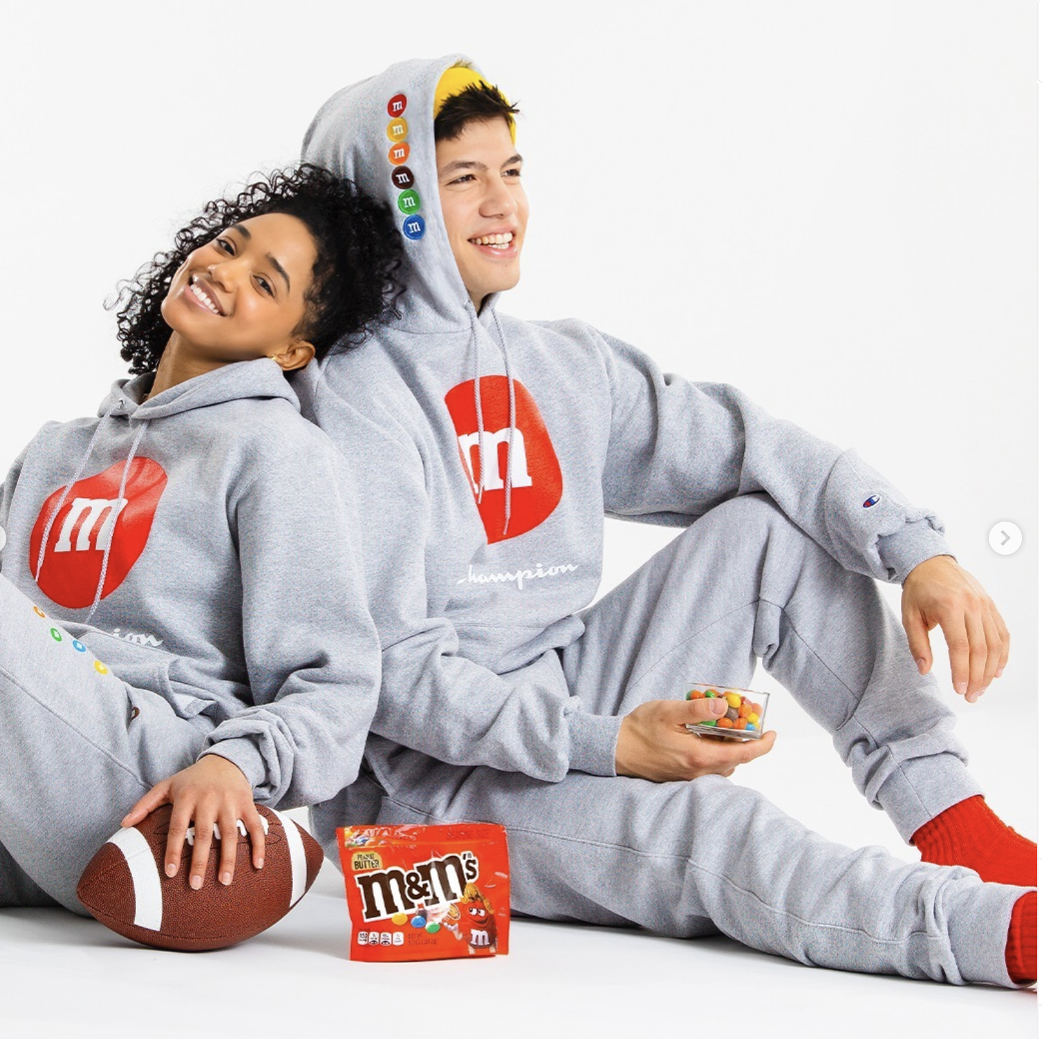 Luke Embers sitting with another model for the Champion x M&M Collaboration.