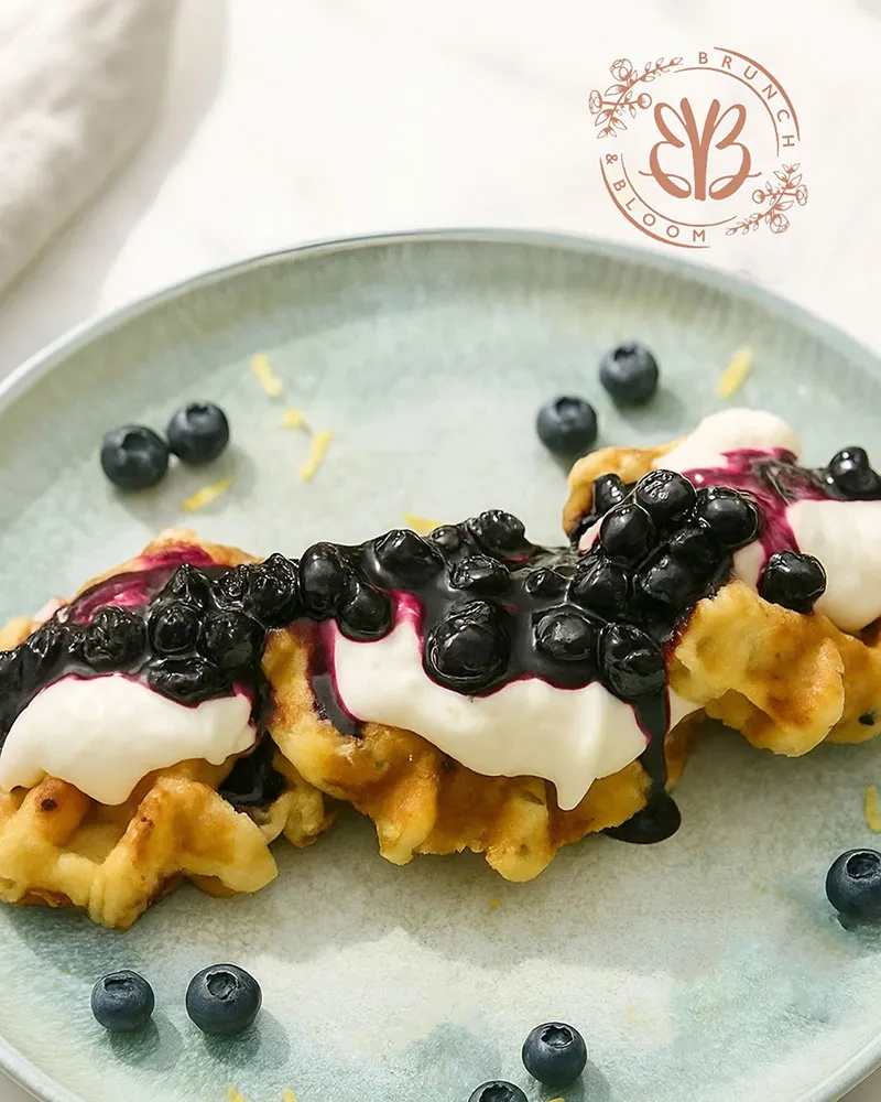 A couple pieces of red velvet waffles with red velvet, blueberry cream, vanilla ice cream and blue berries