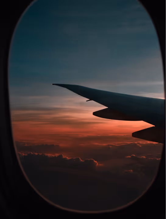 Airplane wing visible through a window with a vibrant sunset sky and clouds below.