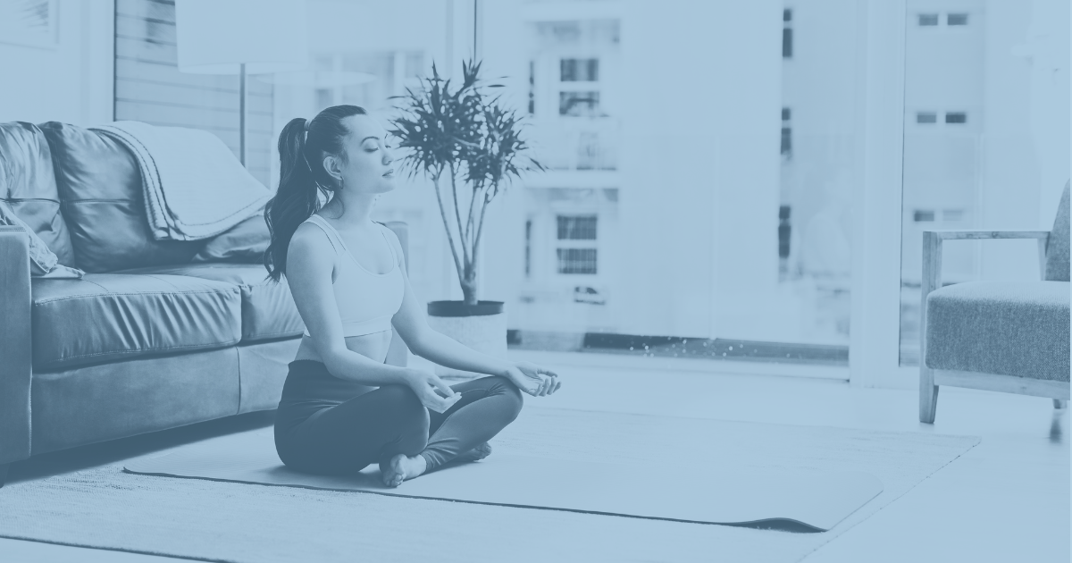 Eine Frau sitzt im Yoga Sitz auf einem Teppich und meditiert mit blauem Filter