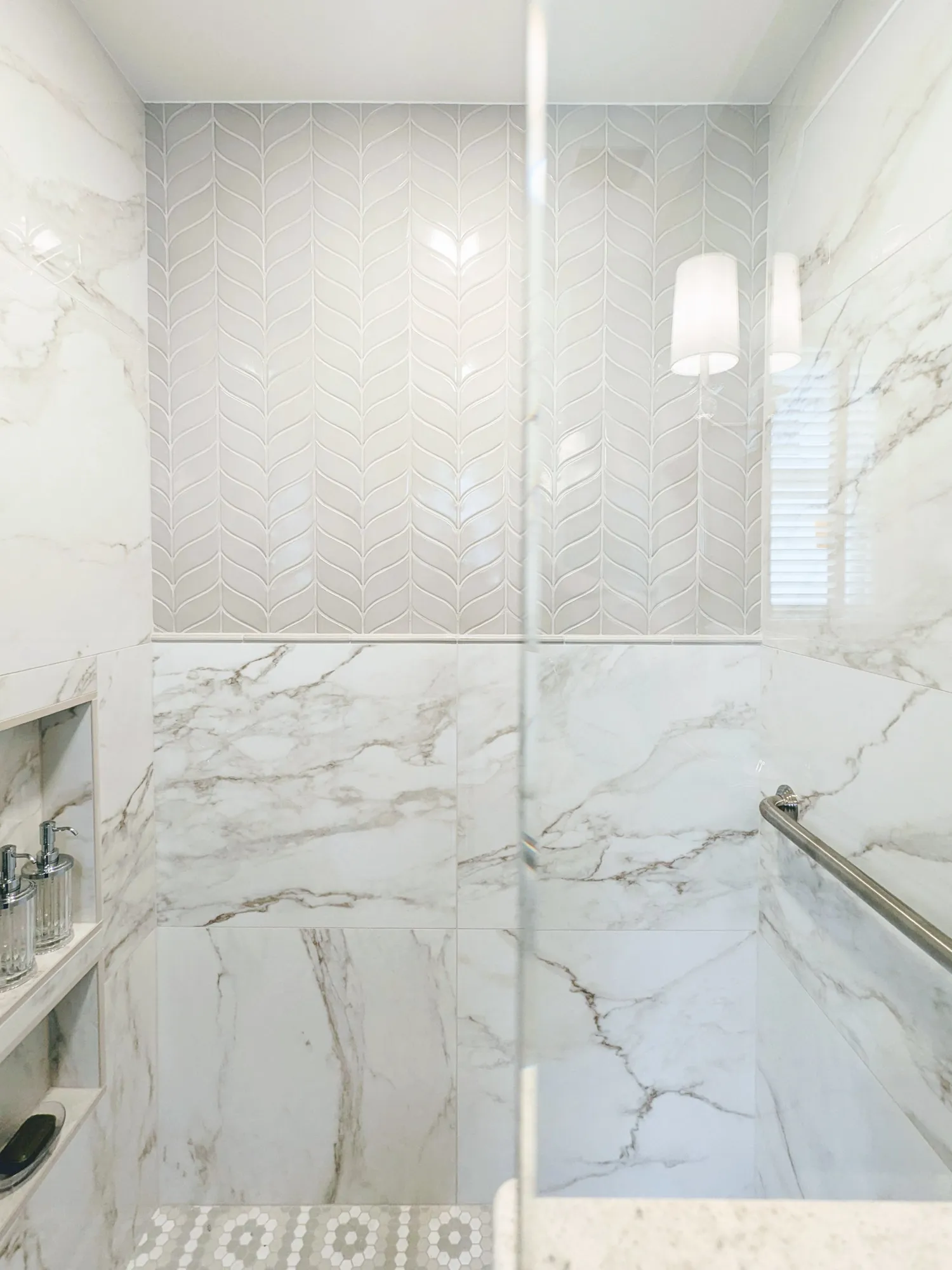 Marble-tiled shower with glass door and built-in shelf