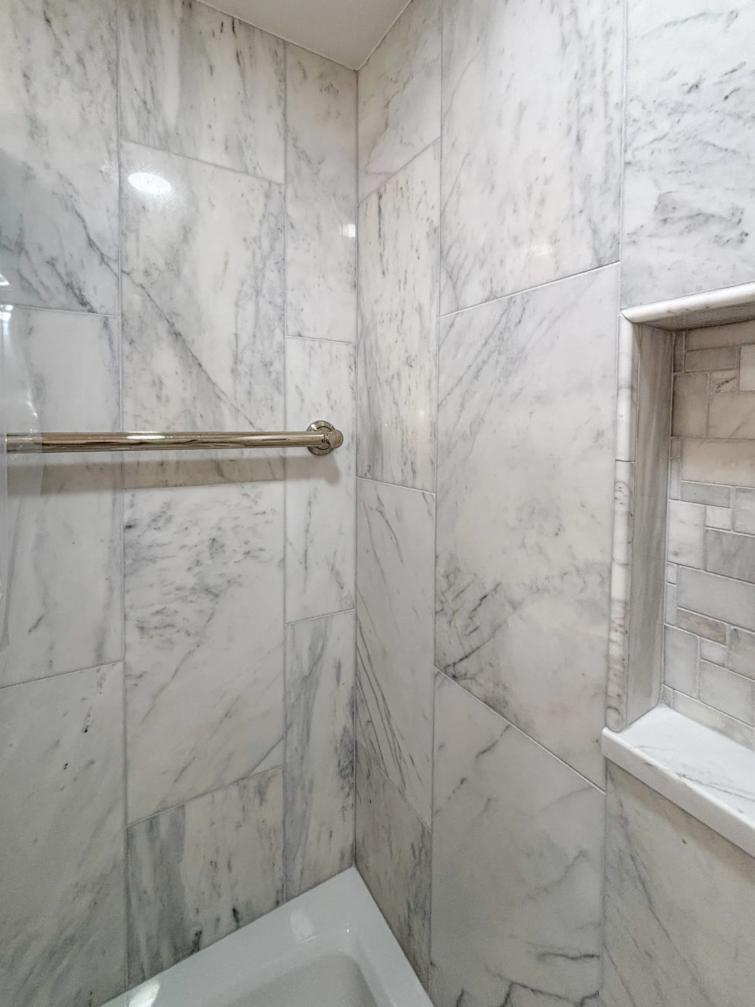 Elegant marble-tiled shower space featuring a built-in niche and sleek chrome fixtures.