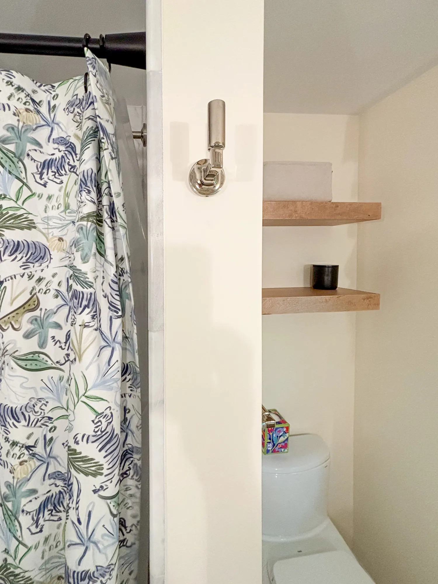 Modern bathroom featuring a floral shower curtain, wooden shelf, and minimalist toilet