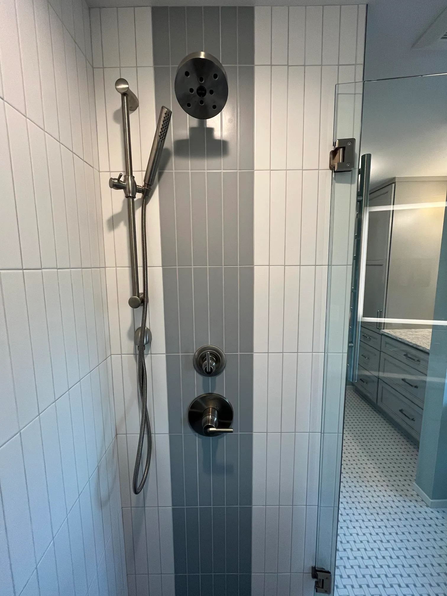 Contemporary bathroom shower with gray and white striped tiles, modern fixtures, and a glass door.