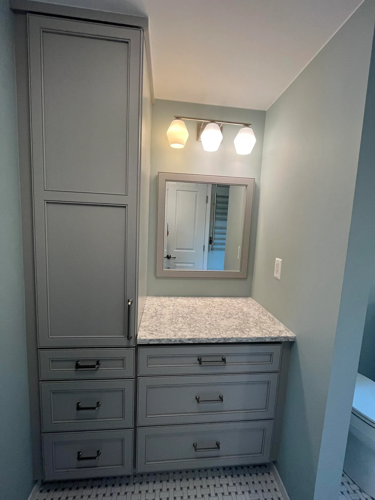 Modern bathroom with gray cabinetry and marble countertop, featuring a stylish mirror and unique light fixtures.