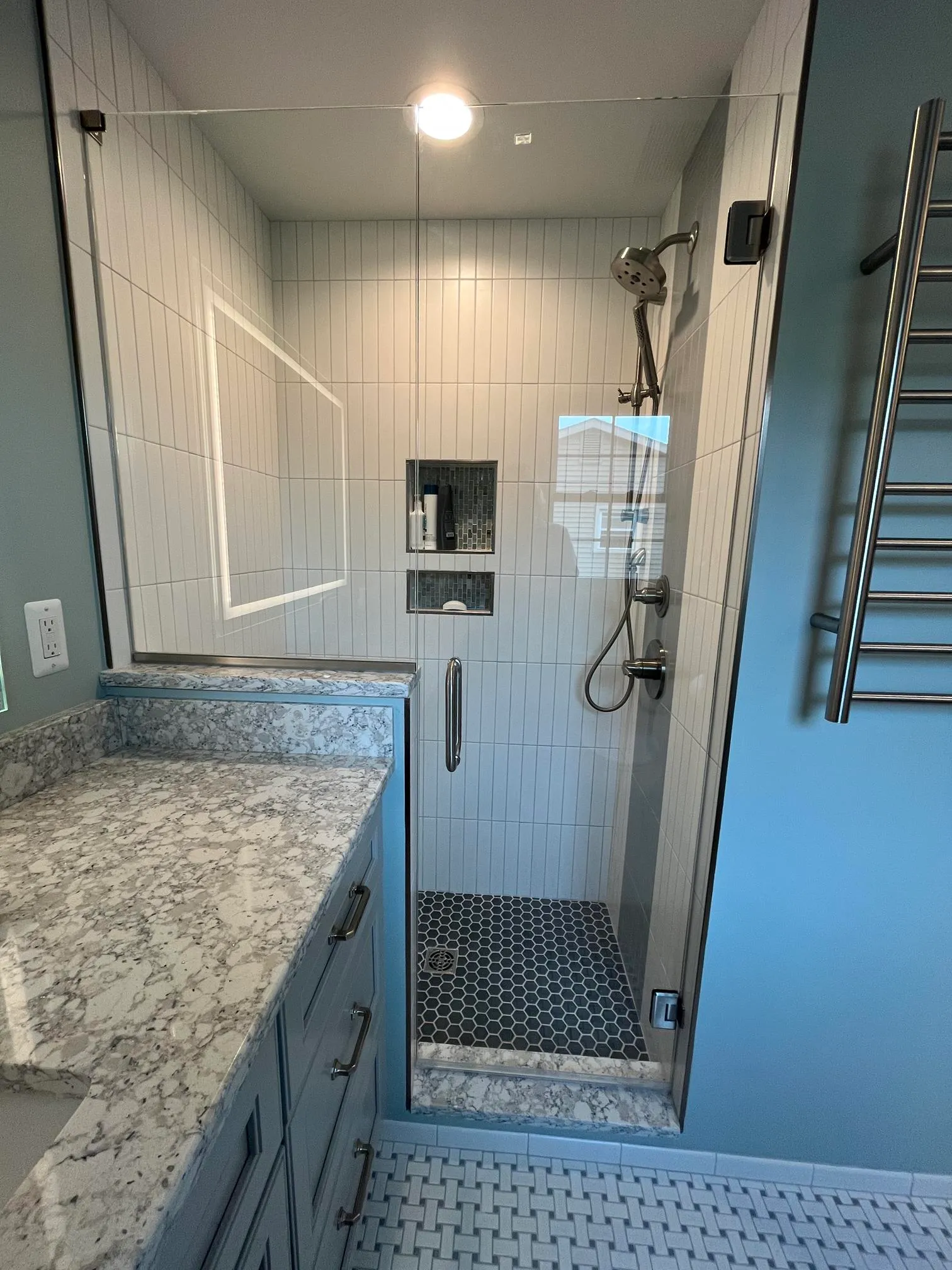 Modern bathroom shower with gray tile, glass enclosure, and hexagonal black tile flooring