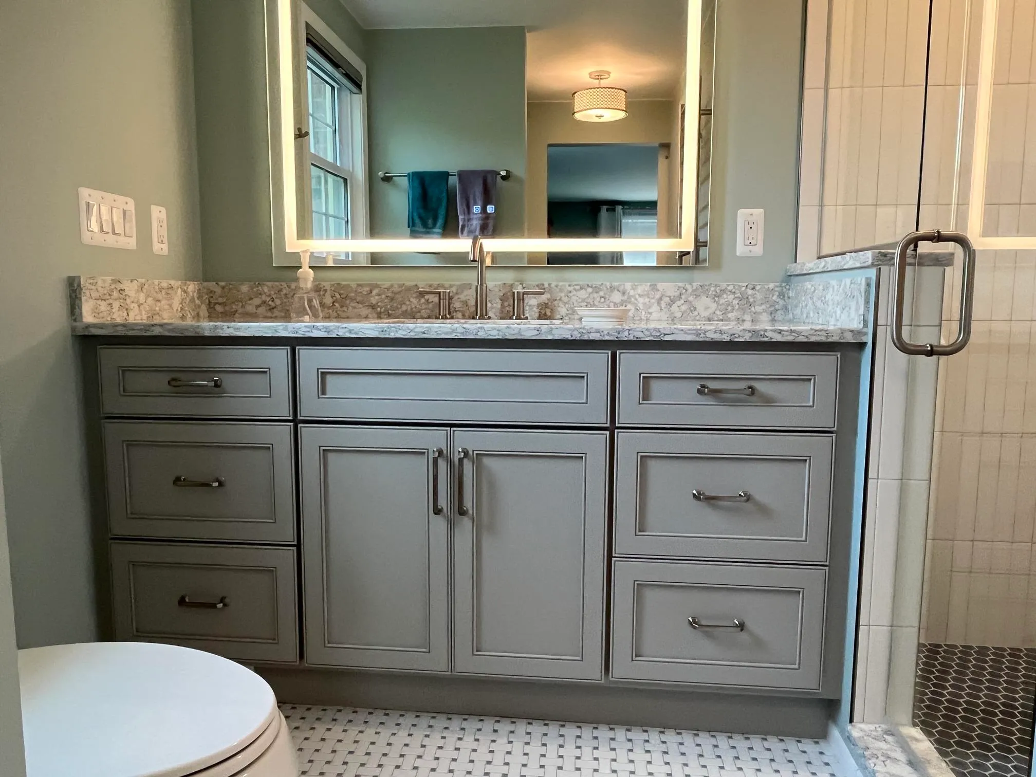Contemporary bathroom featuring gray cabinets, a marble countertop, and a glass shower enclosure.