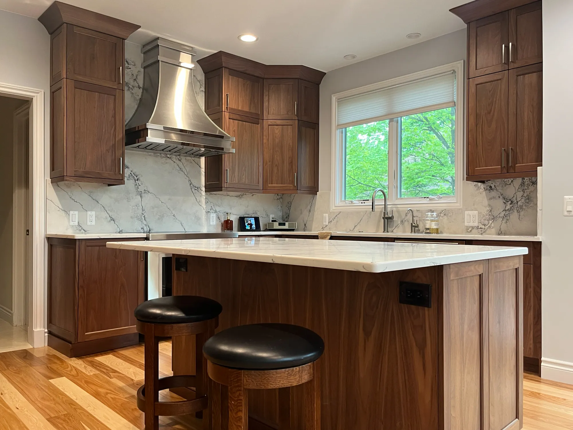 Modern kitchen in plymouth michigan featuring rich wood cabinets, a marble backsplash, and an island with bar stools.