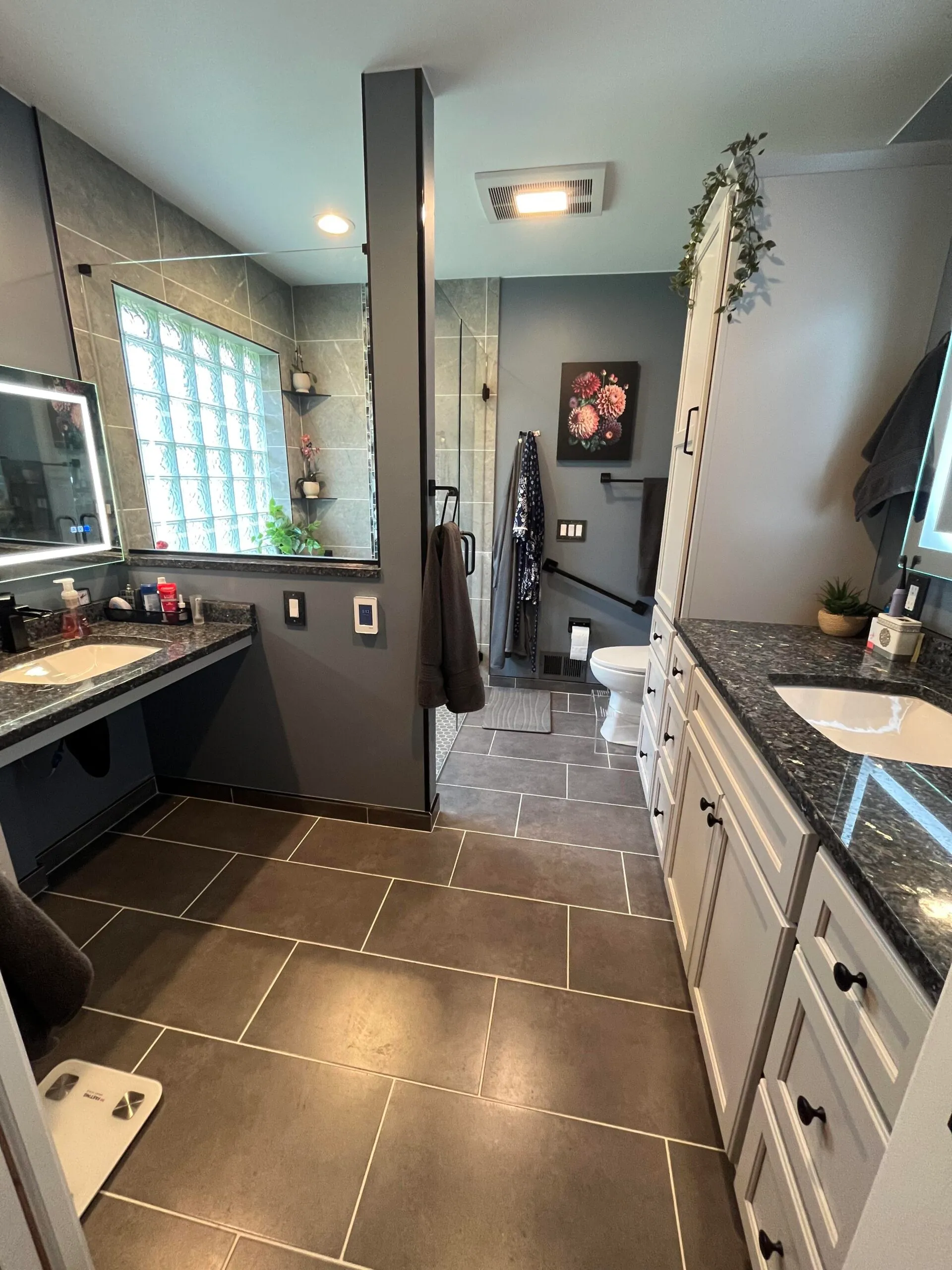 Modern bathroom featuring a granite countertop, dark tile flooring, and glass block window.