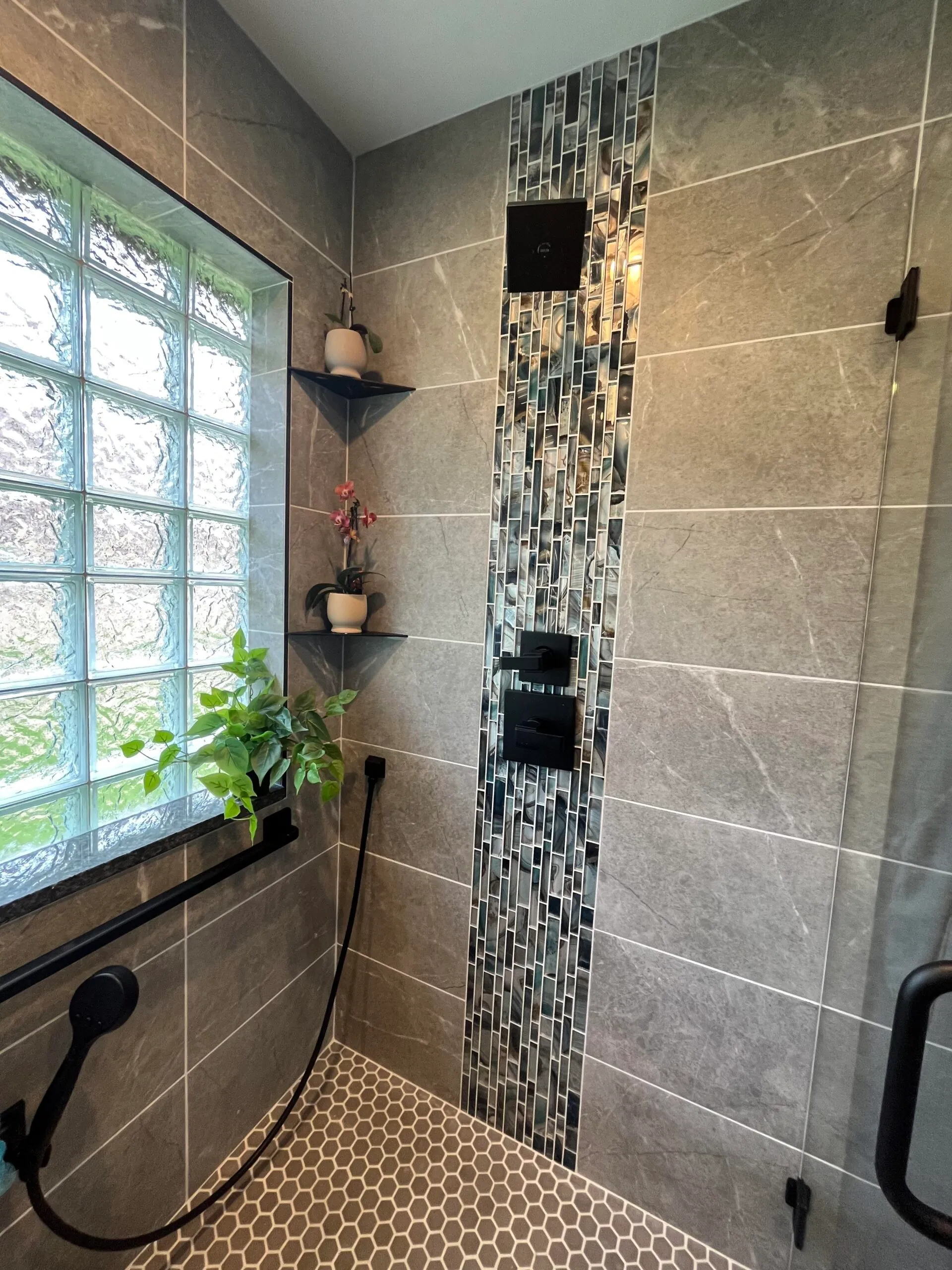 Modern bathroom shower featuring gray tiles, patterned flooring, and glass block window.