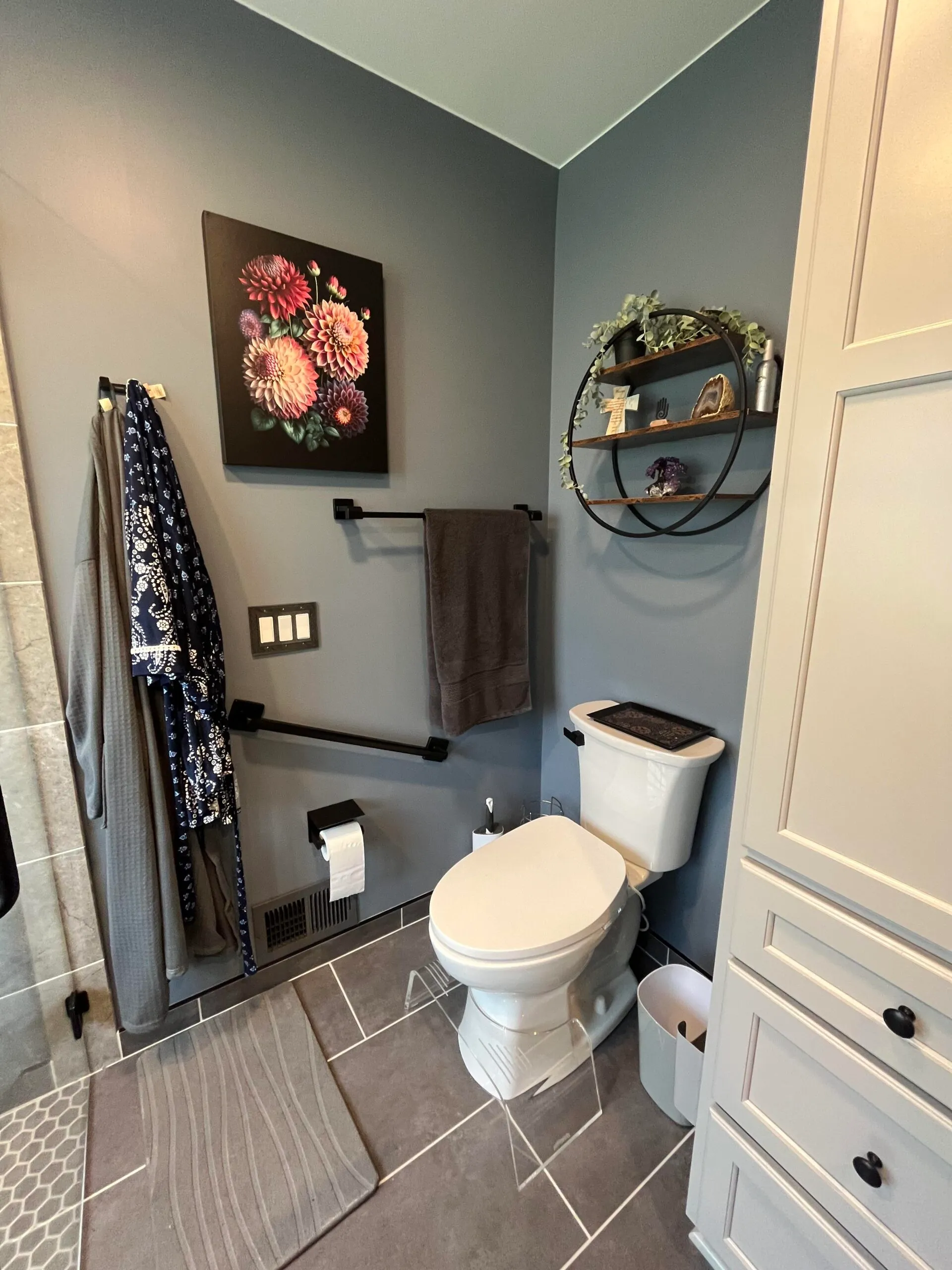 Modern bathroom with gray walls, a white toilet, grab bars, and floral wall art in Plymouth.