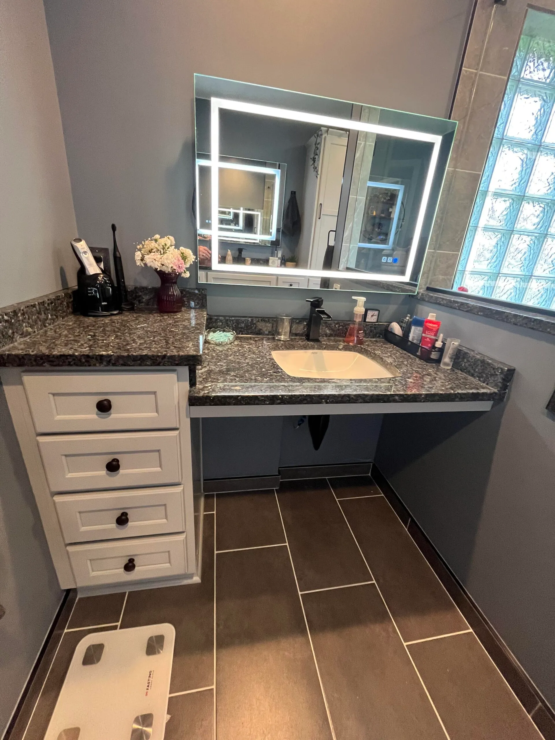 Modern bathroom featuring a roll-under vanity with a granite countertop, illuminated mirror, and sleek black fixtures.