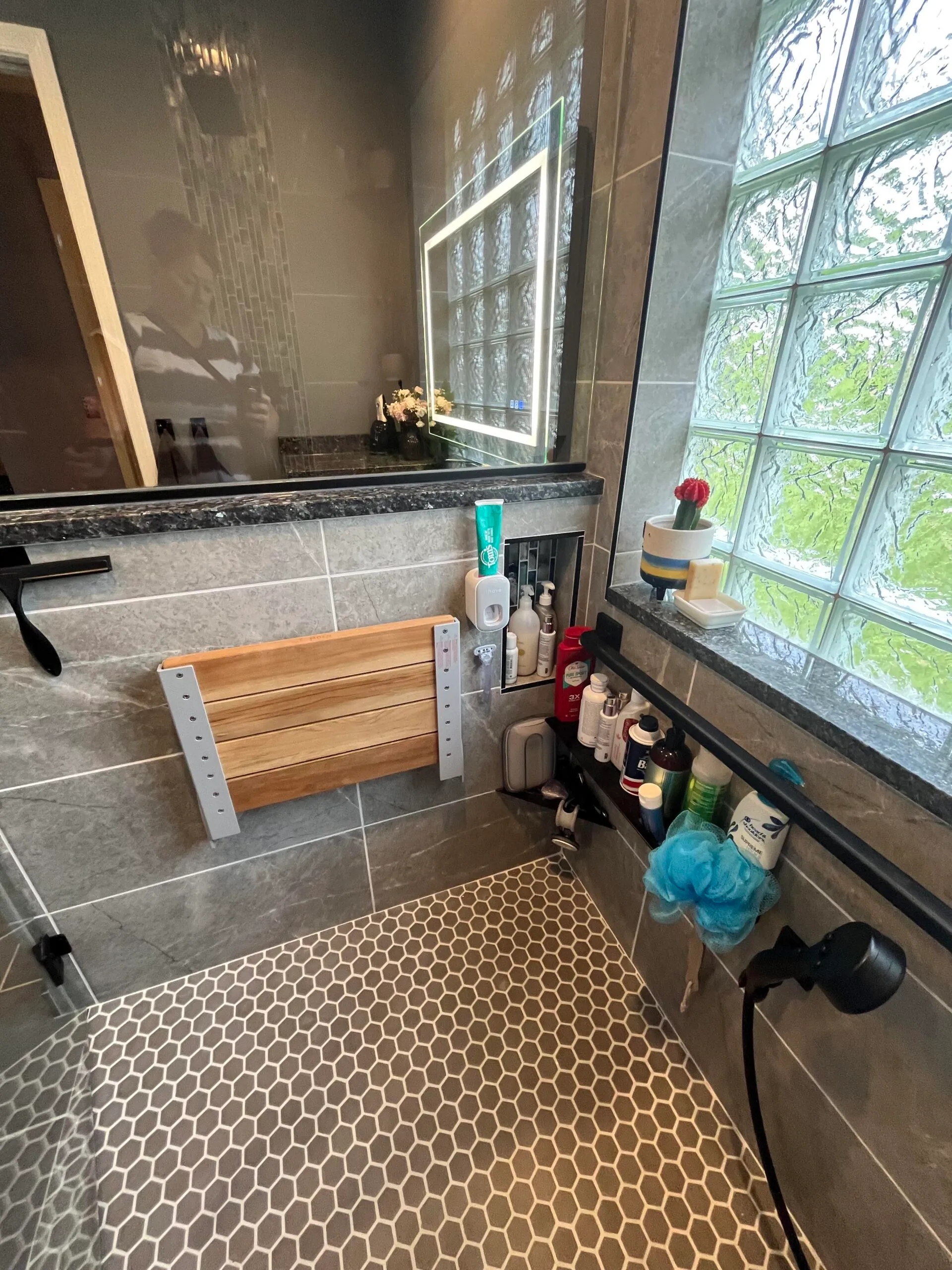 Modern bathroom with a hexagonal tile shower floor, glass block window, and a wooden bath seat.
