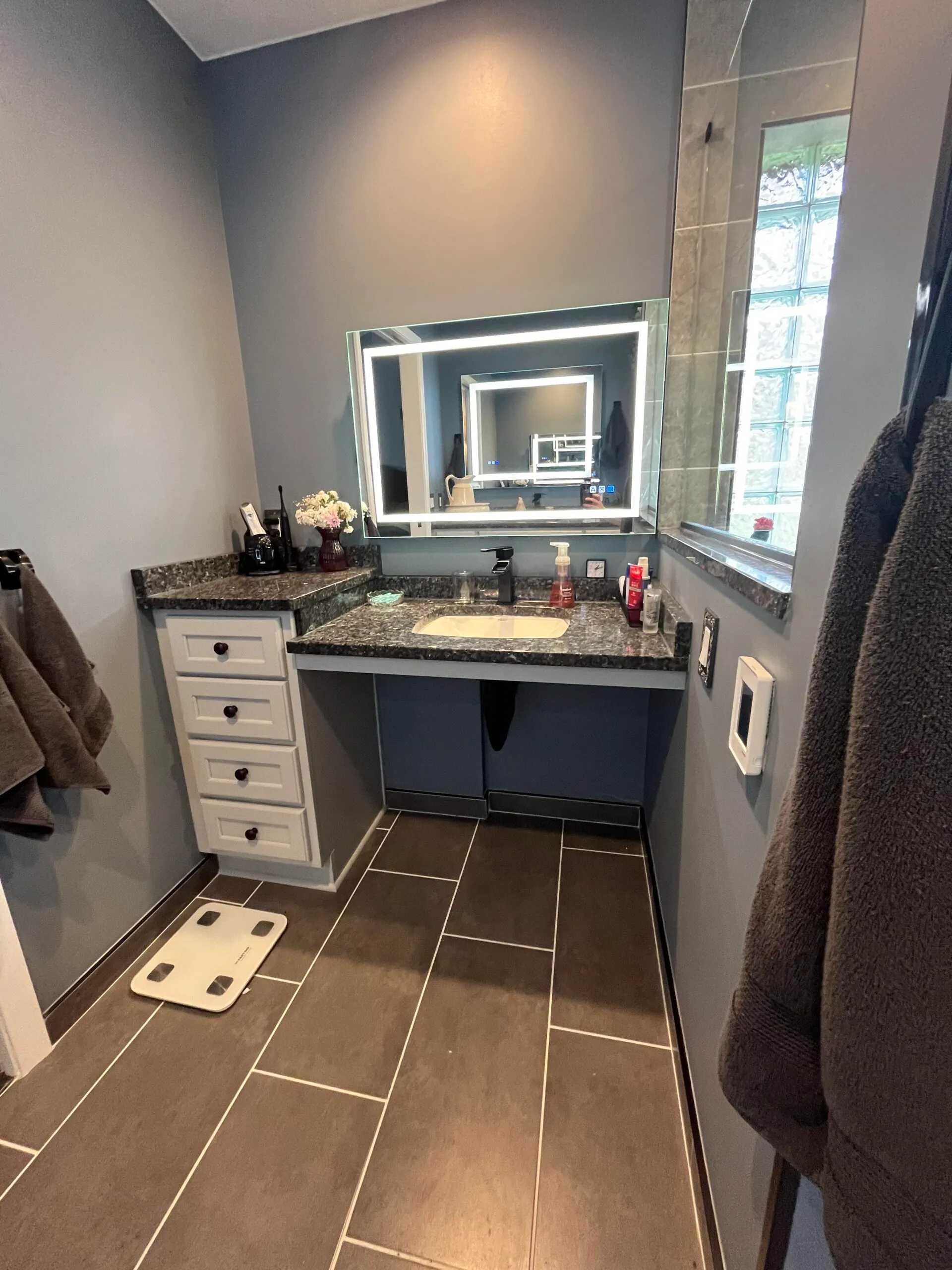 Modern bathroom featuring a roll-under vanity with a granite countertop and sleek mirror, designed for accessibility.