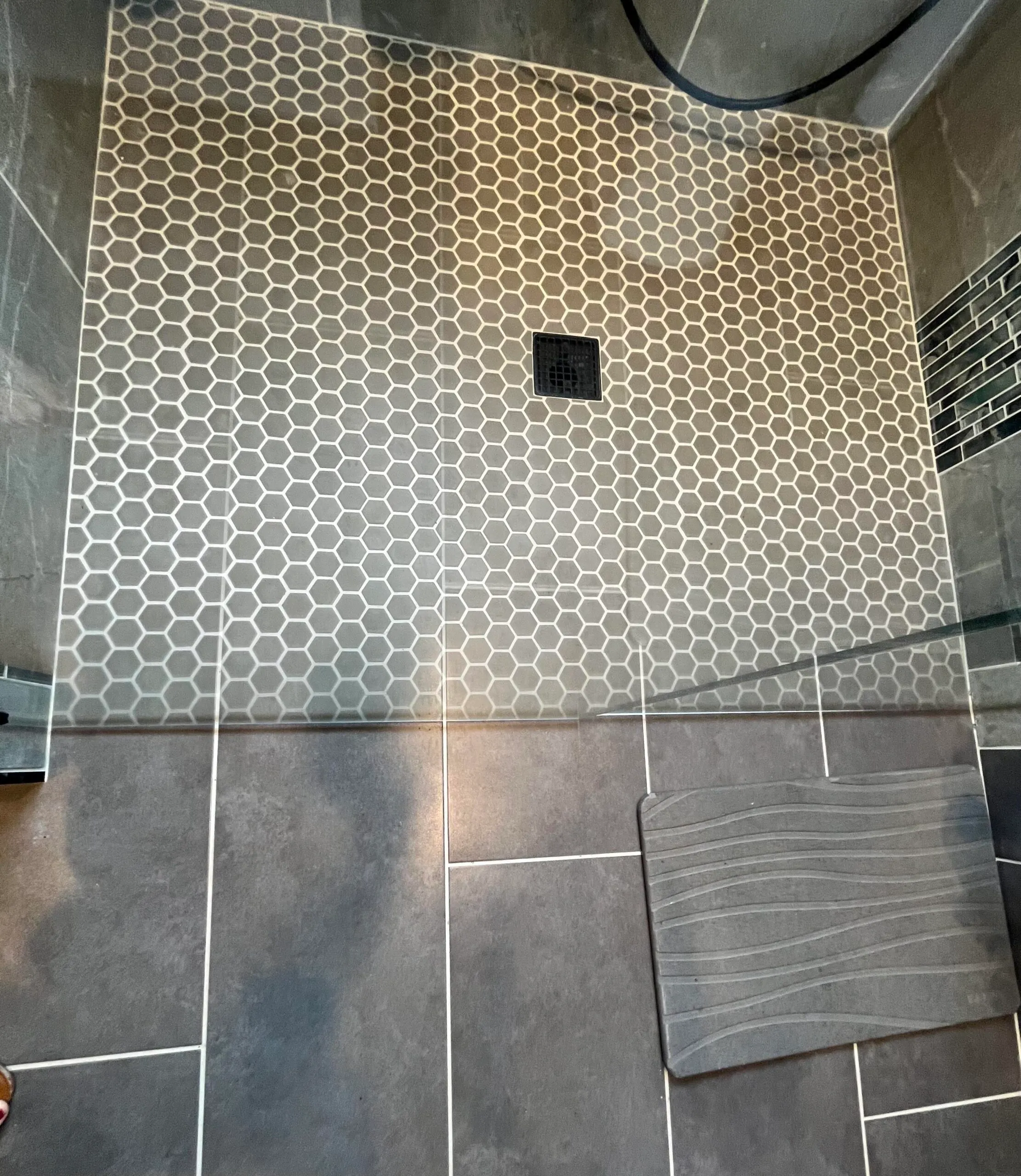 Modern bathroom shower featuring hexagonal tile flooring and a sleek gray mat in a contemporary aesthetic
