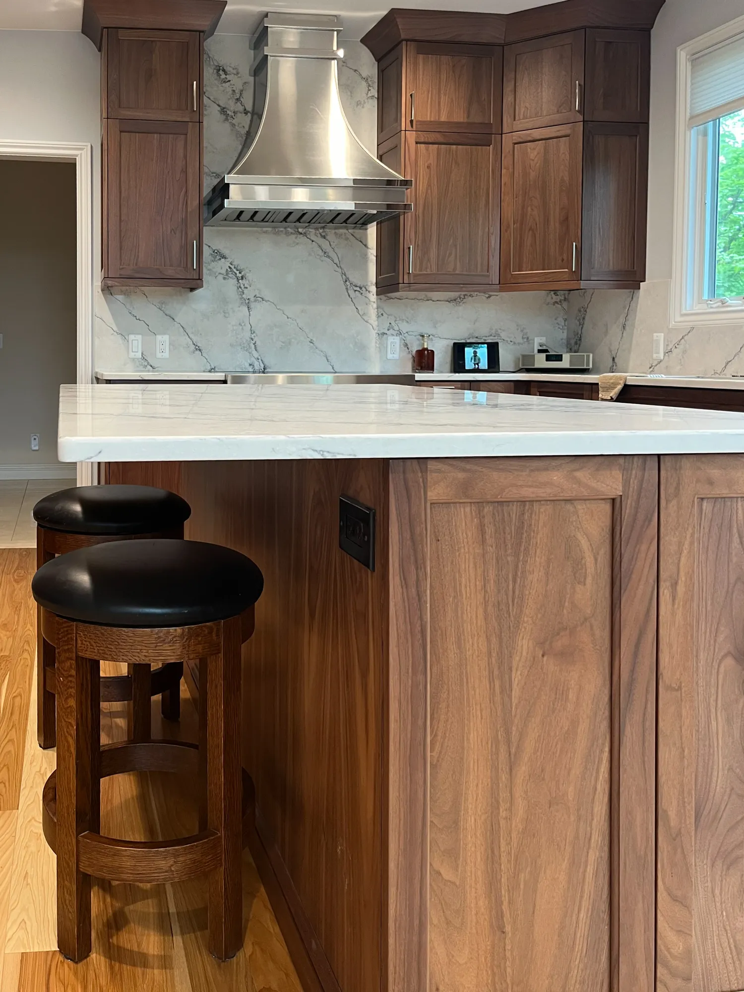 Modern kitchen renovation in plymouth, michigan featuring walnut cabinets, marble backsplash, and elegant bar stools.