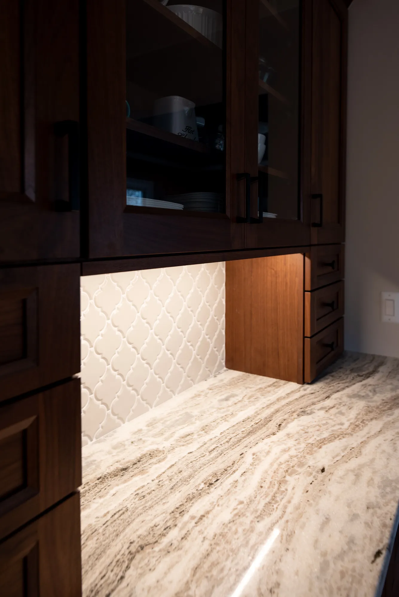 Modern kitchen with dark wood cabinets and a glossy white backsplash, featuring a beautiful marble countertop.